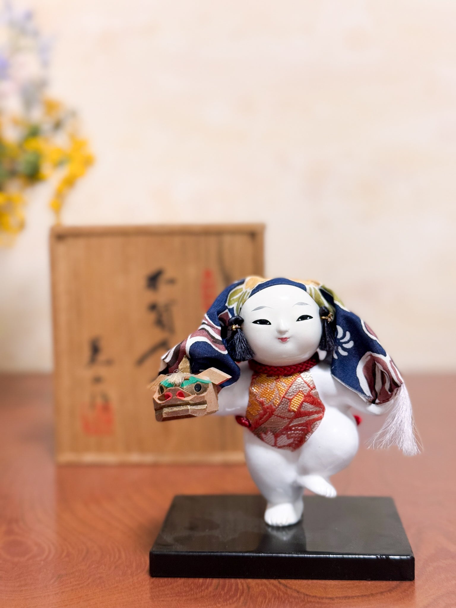 Figurine japonaise Gosho Ningyō représentant un enfant dansant avec une tête de lion Shishimai, sur socle laqué, avec boîte en bois calligraphiée, vu de face