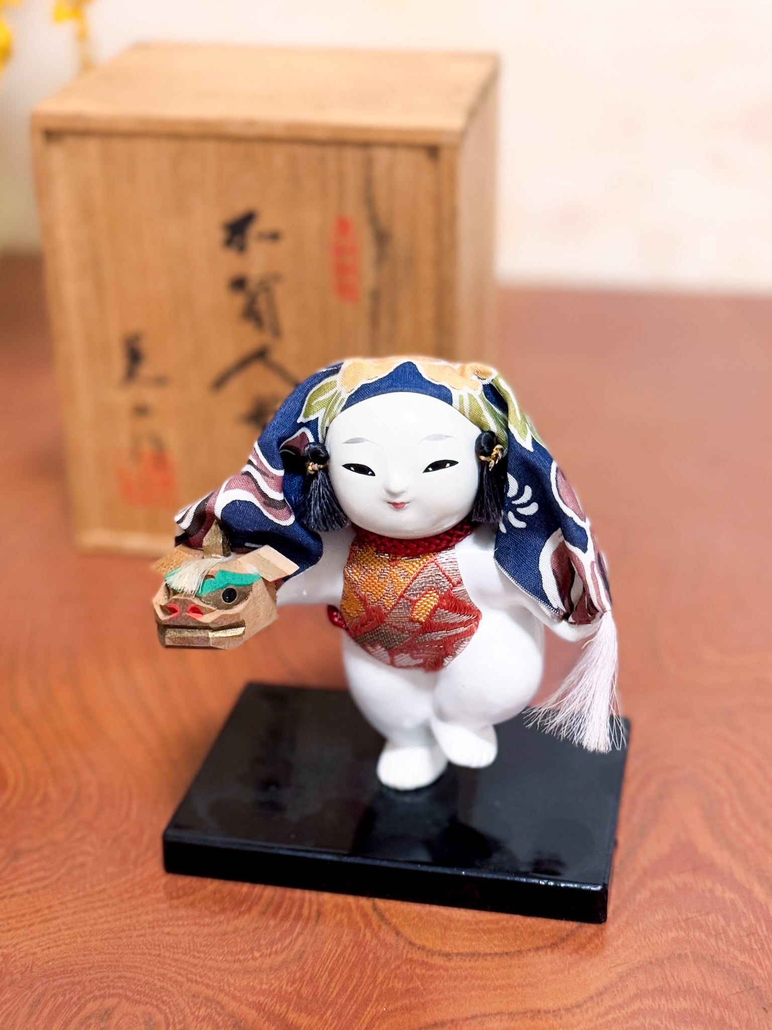 Figurine japonaise Gosho Ningyō représentant un enfant dansant avec une tête de lion Shishimai, sur socle laqué, avec boîte en bois calligraphiée, vu de dessus