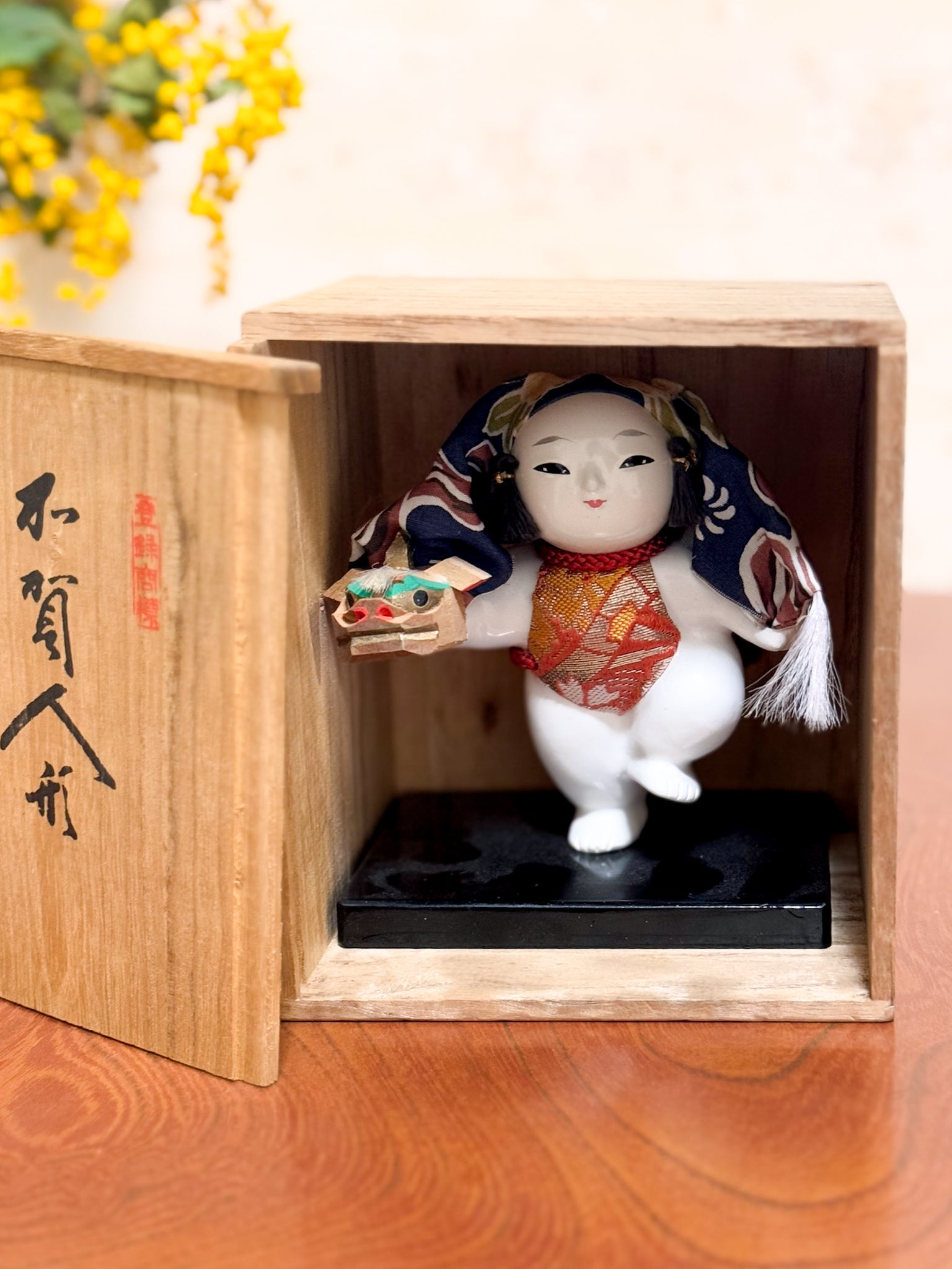 Figurine japonaise Gosho Ningyō représentant un enfant dansant avec une tête de lion Shishimai, sur socle laqué, avec boîte en bois calligraphiée, vu dans sa boite