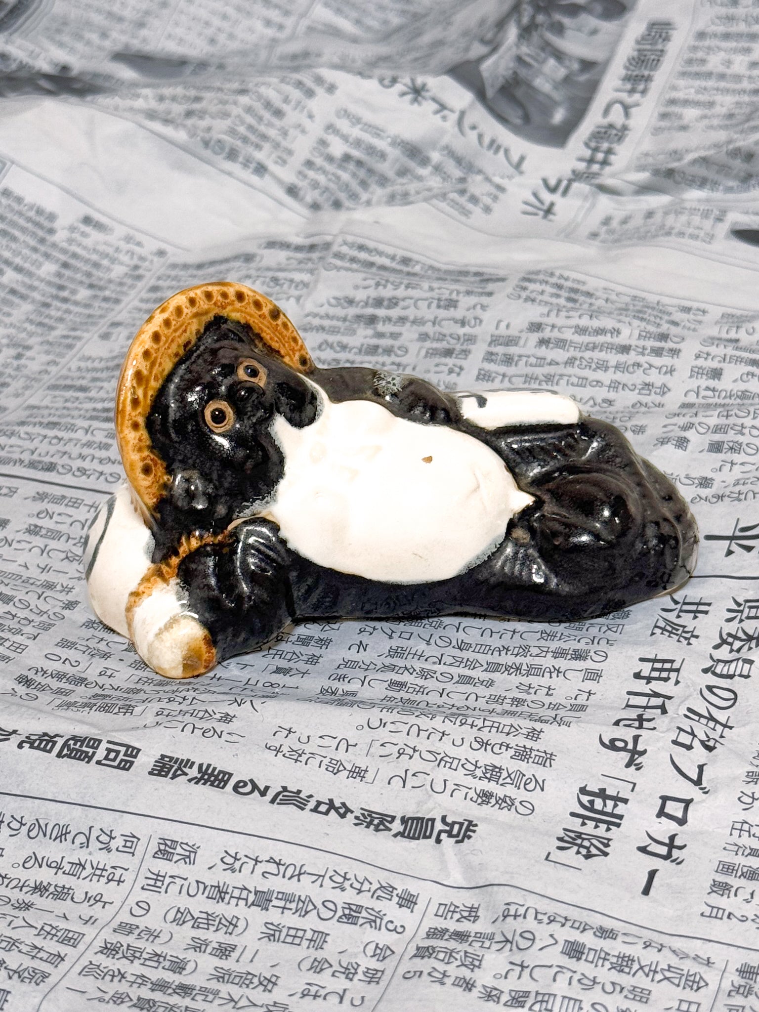 Figurine en céramique d’un tanuki allongé sur une bouteille de saké portant le kanji 福, symbole de bonheur et de prospérité au Japon