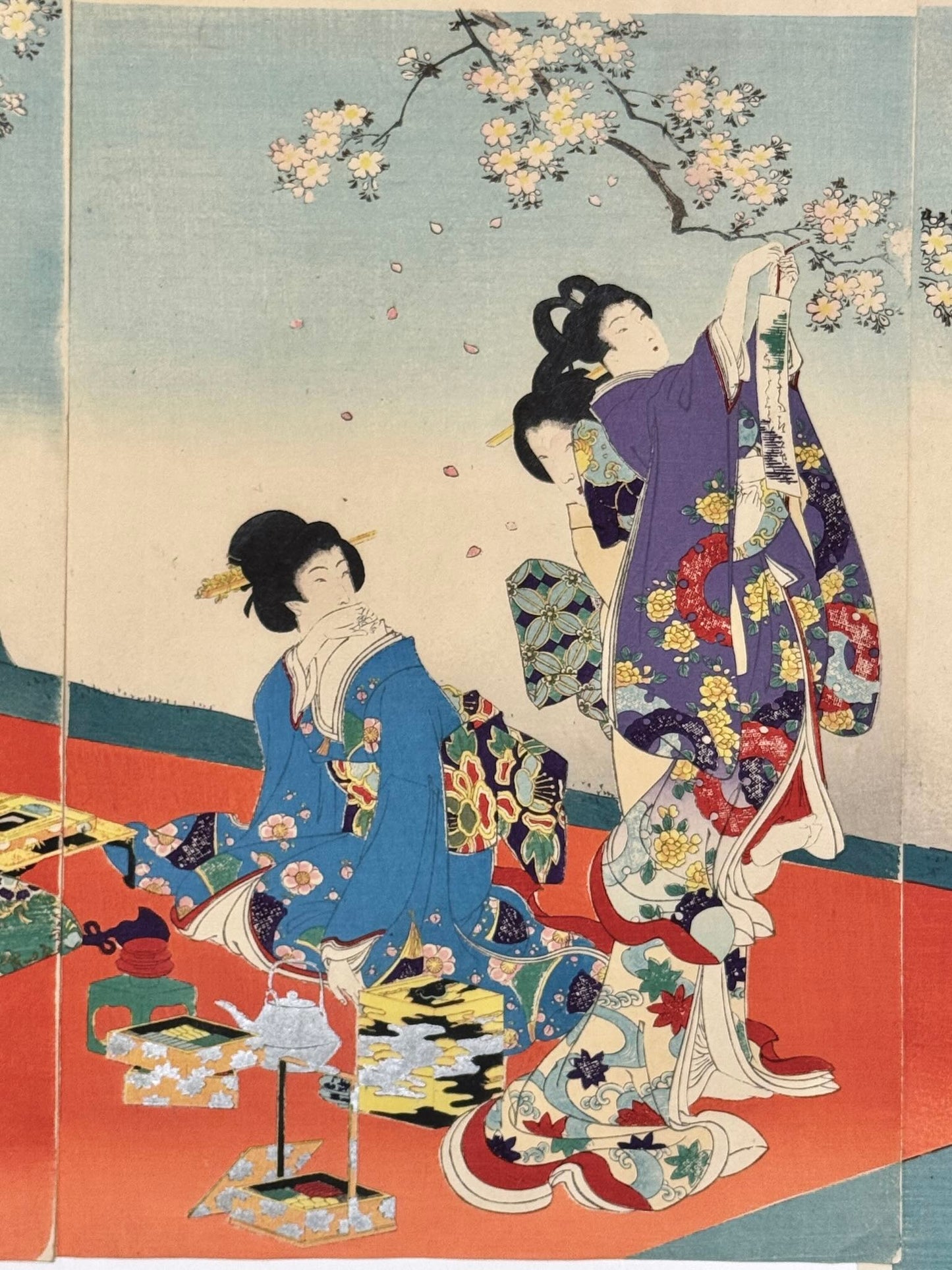 Estampe Japonaise triptyque de Chikanobu représentant des dames de la cour des Tokugawa célébrant le hanami sous des cerisiers en fleurs, détail du panneau central, dame assise devant des laques tandis qu'une autre accroche un poème sur une branche de cerisier en fleurs