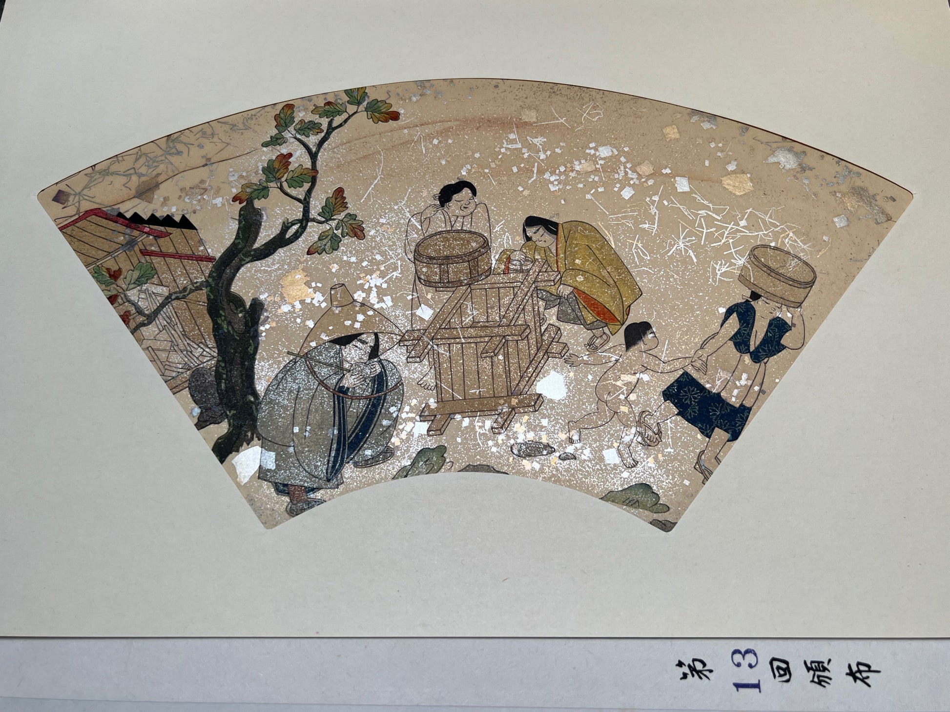 Estampe japonaise en forme d'éventail parsemée de fragments d'or et d'argent, femmes et enfant près d'un puits, sous un chêne, série sutra du lotus n°13 écrit en japonais coin inférieur droit.