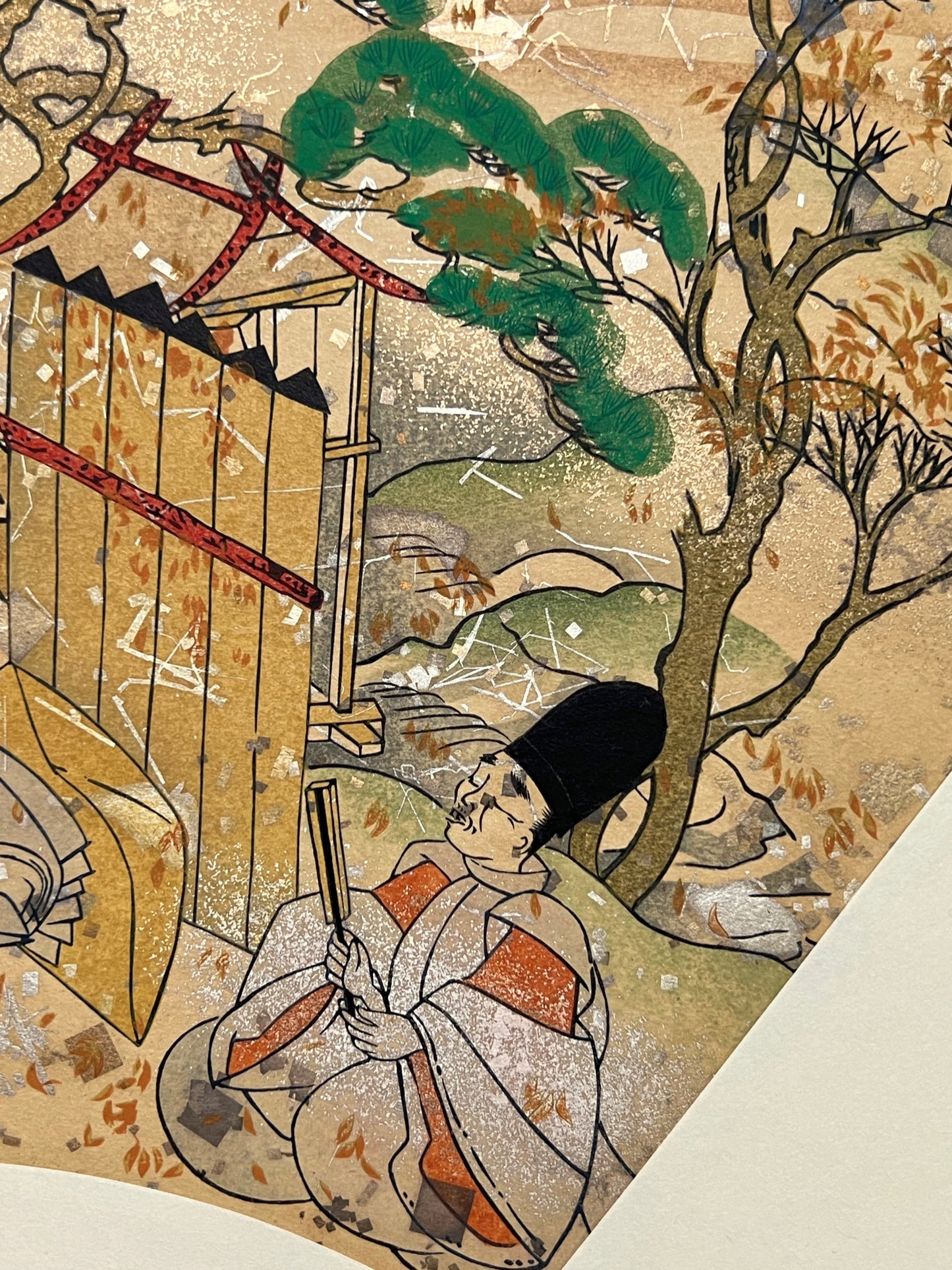 Estampe japonaise en forme d'éventail parsemée de fragments d'or et d'argent, gros plan sur un homme qui chante, clôture et toit traditionnel, pin.