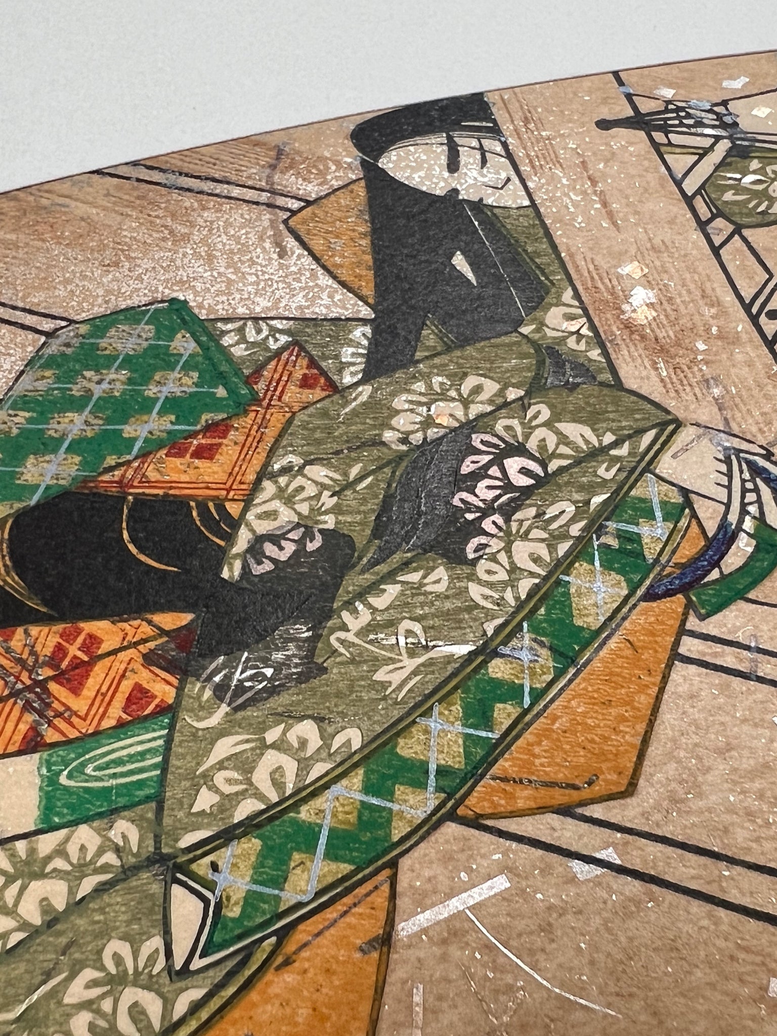 Estampe japonaise en forme d'éventail parsemée de fragments d'or et d'argent, gros plan sur la manche droite du kimono de la femme assoupie sur la terrasse.