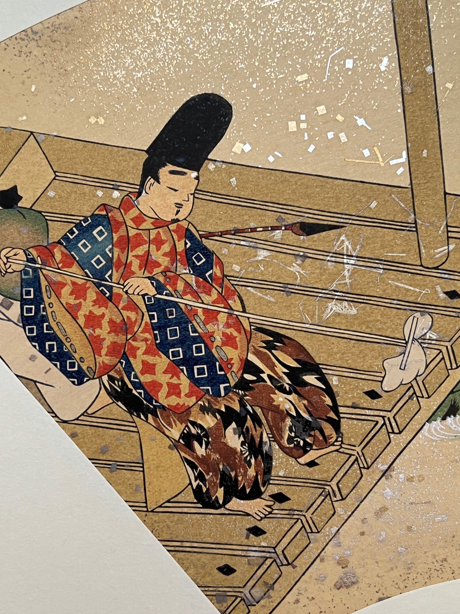 Estampe japonaise en forme d'éventail parsemée de fragments d'or et d'argent, gros plan sur l'homme passant la serpillère sur la terrasse à gauche de l'estampe.