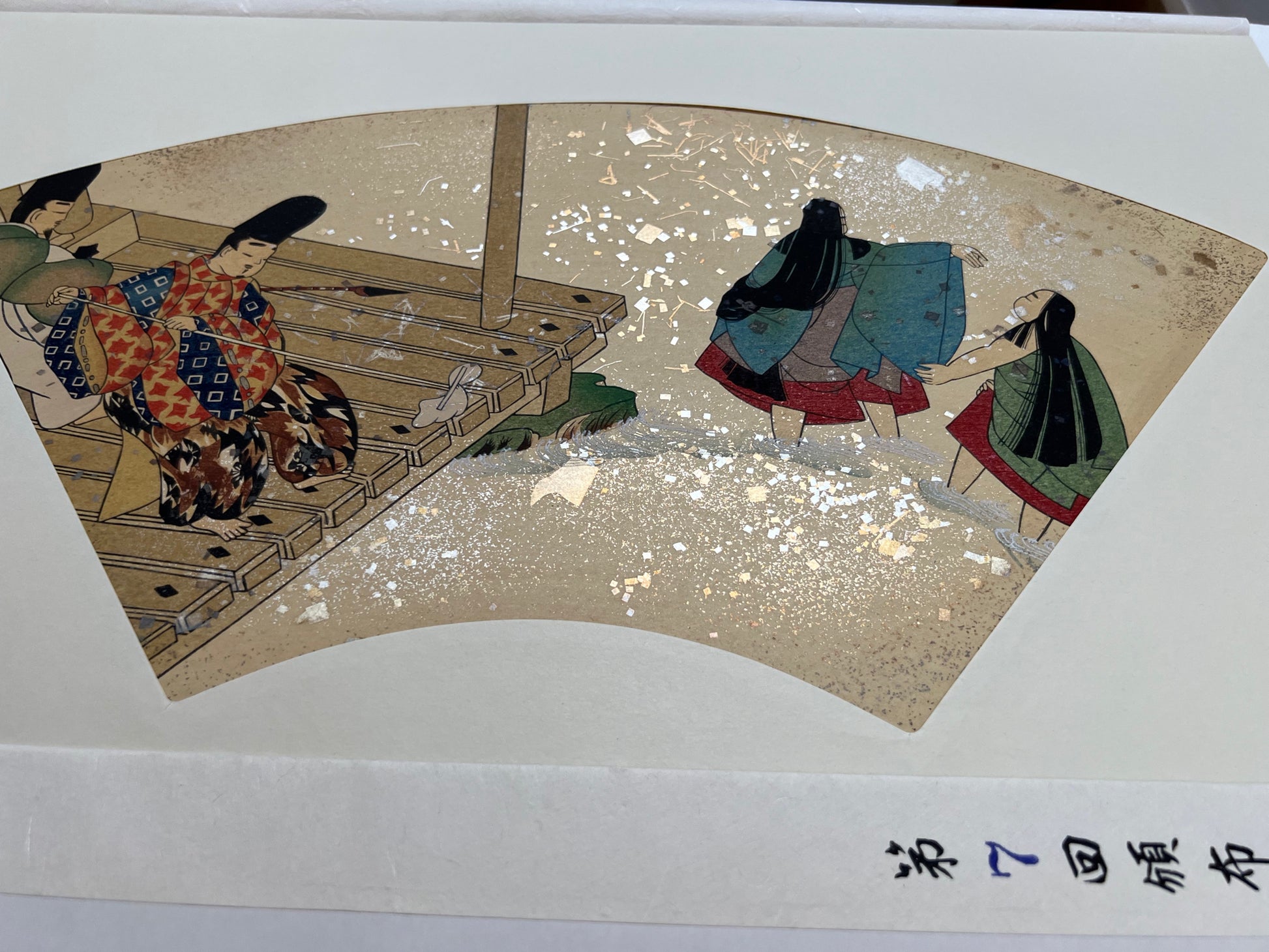 Estampe japonaise en forme d'éventail parsemée de fragments d'or et d'argent, deux hommes nettoient une terrasse au bord de l'eau pendant que deux femmes se baignent dans la rivière, série sutra du lotus n°7 écrit en japonais dans le coin inférieur droit.