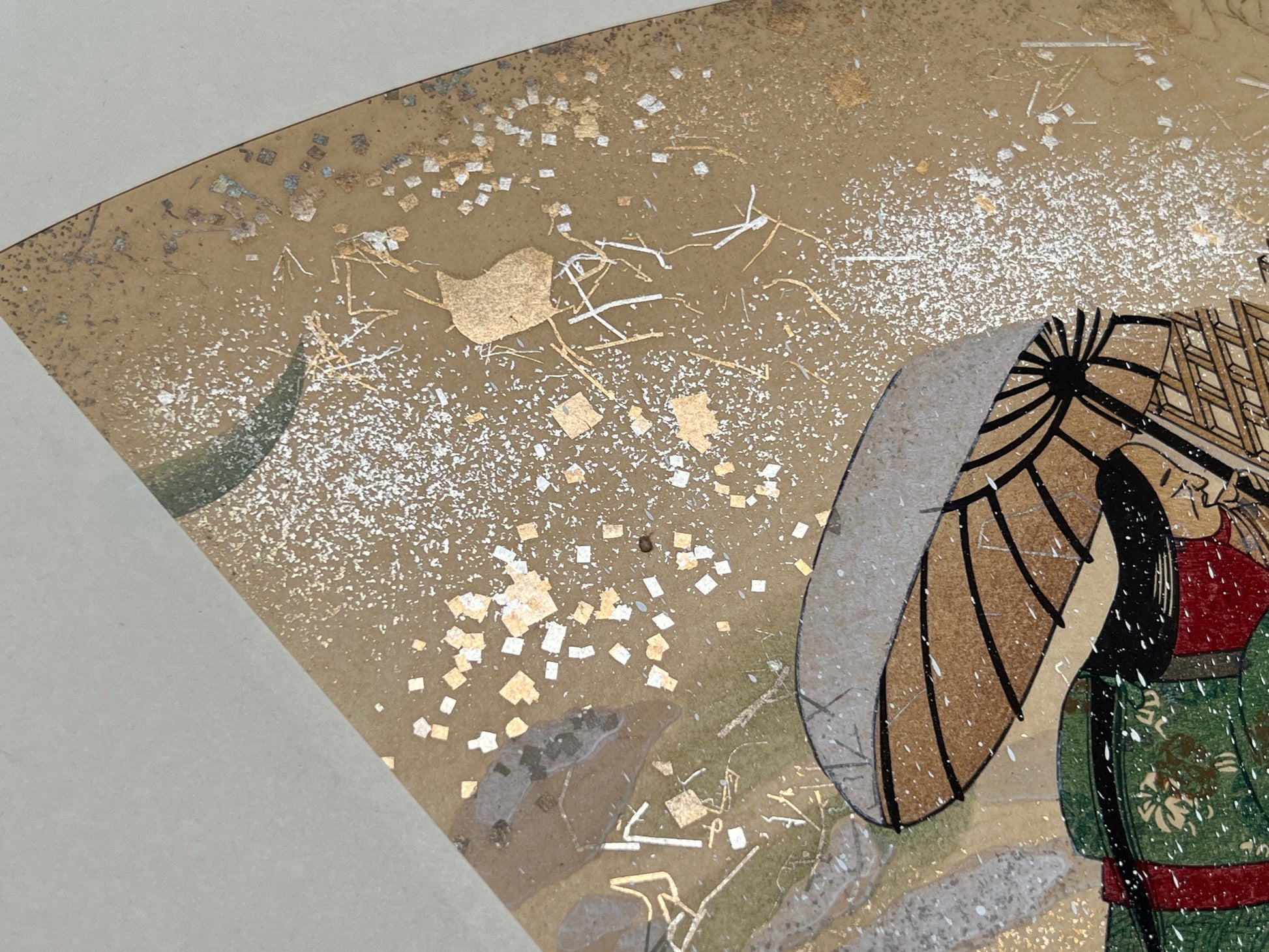 Estampe japonaise en forme d'éventail parsemée de fragments d'or et d'argent, matin neigeux, coin supérieur gauche, neige, fragments scintillants, vieille femme sous une ombrelle.
