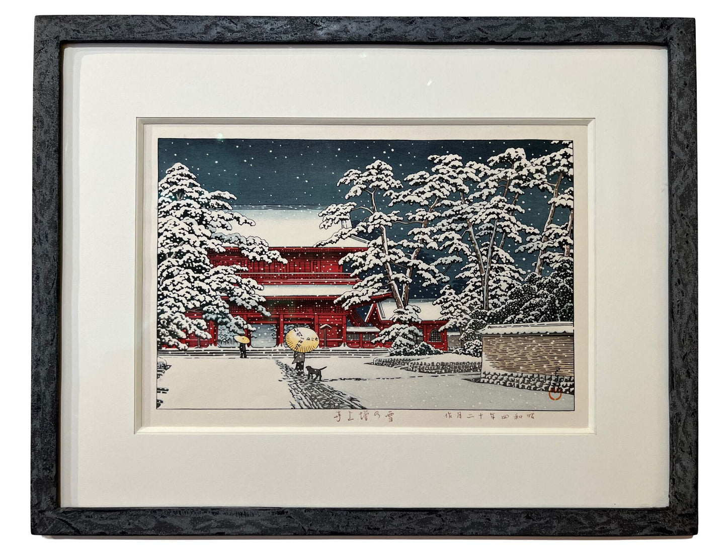 estampe japonaise encadrée paysage hiver, la neige tombe la nuit sur le temple rouge, des personnes sous un parapluie avec un chien