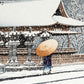 estampe japonaise neige tombant sur pagode rouge personnage sous parapluie, en kimono bleu parapluie jaune