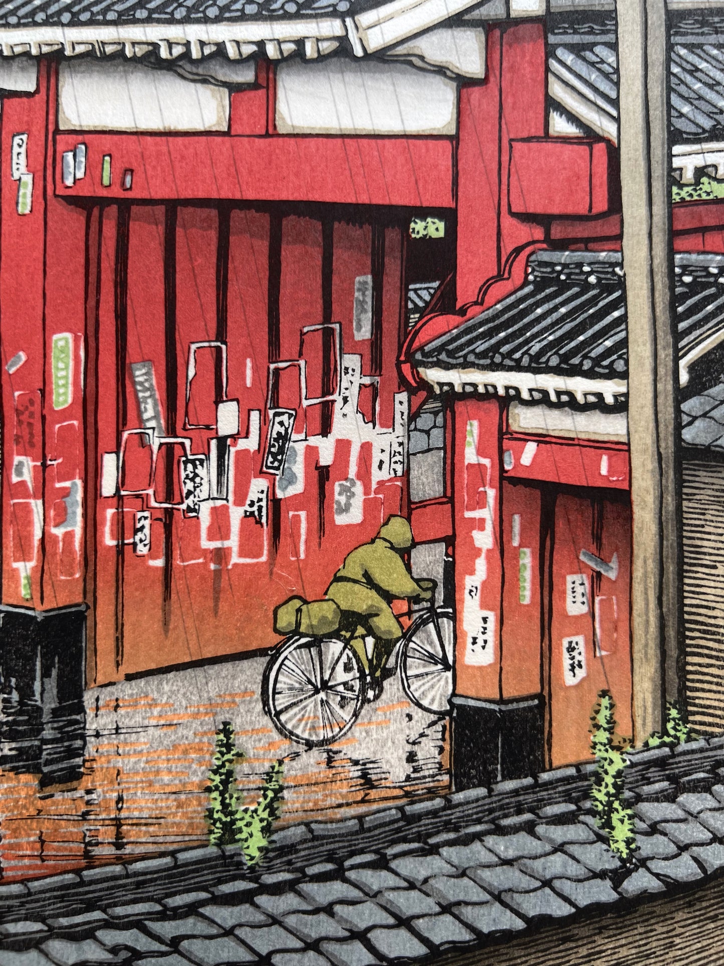 estampe japonaise un personnage à vélo franchit la grande porte rouge d'un temple sous la pluie à Tokyo, détail personnage en ciré vert à vélo
