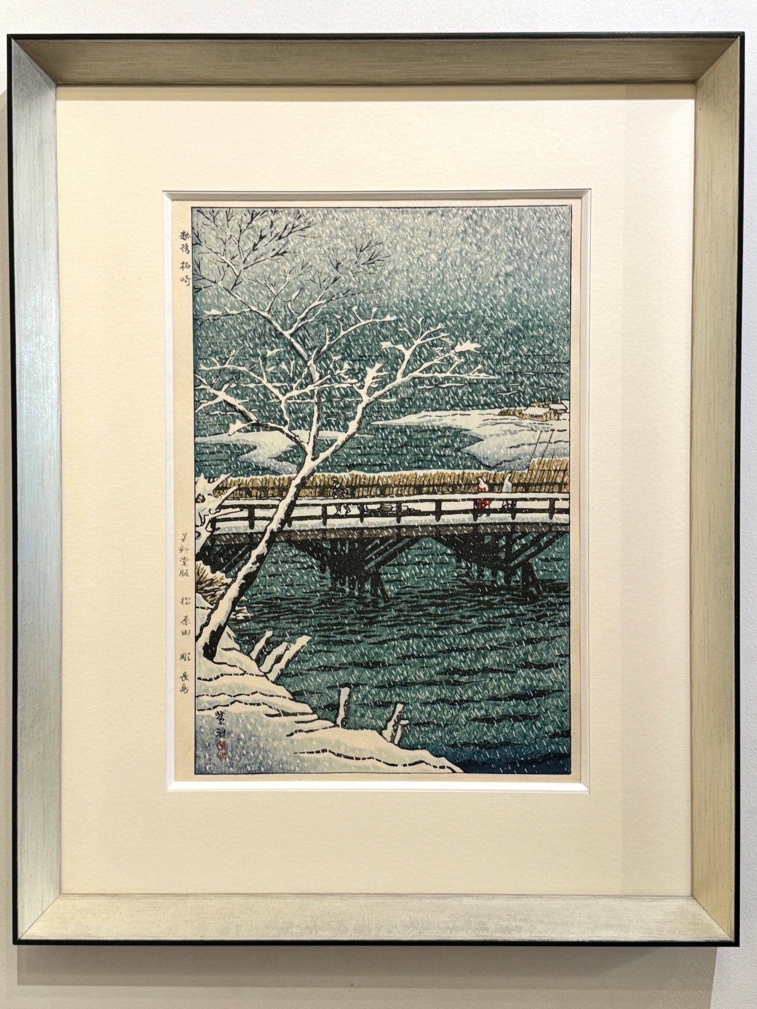 estampe japonaise  de neige de kasamatsu personnage sur un pont en pleine tempête de neige, un exemple d'encadrement noir et argent