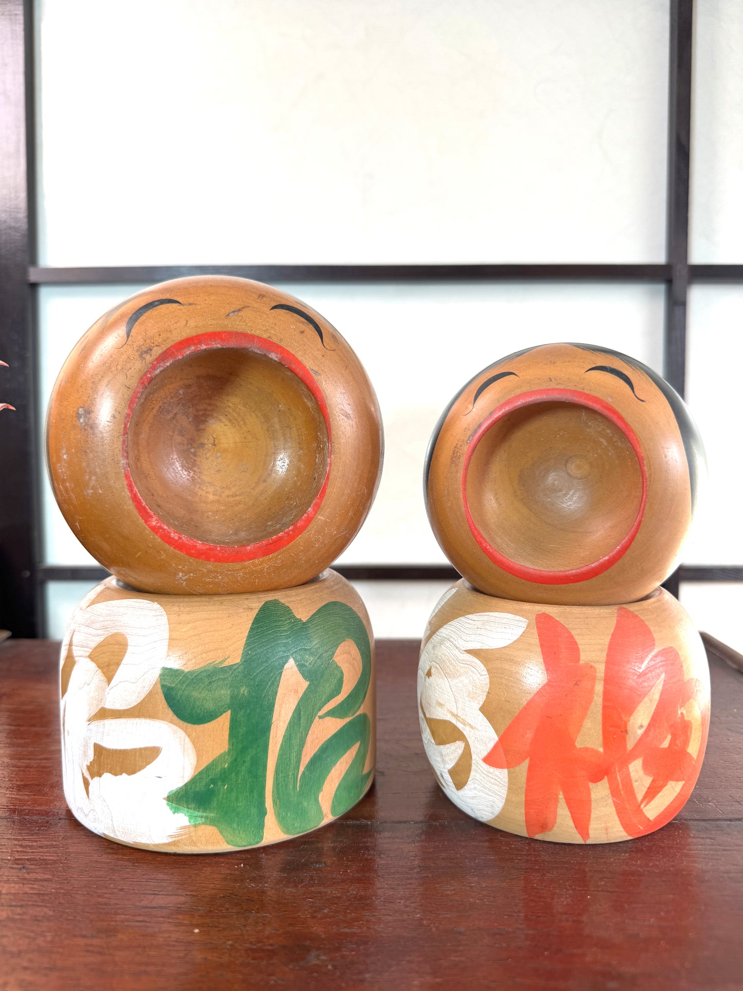 Couple de kokeshi rieuses en bois, calligraphie rouge et verte, signées Sato Kouson vu de face