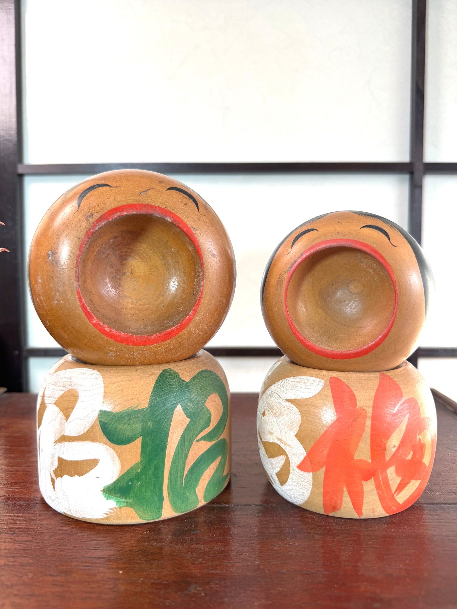 Couple de kokeshi rieuses en bois, calligraphie rouge et verte, signées Sato Kouson vu de face