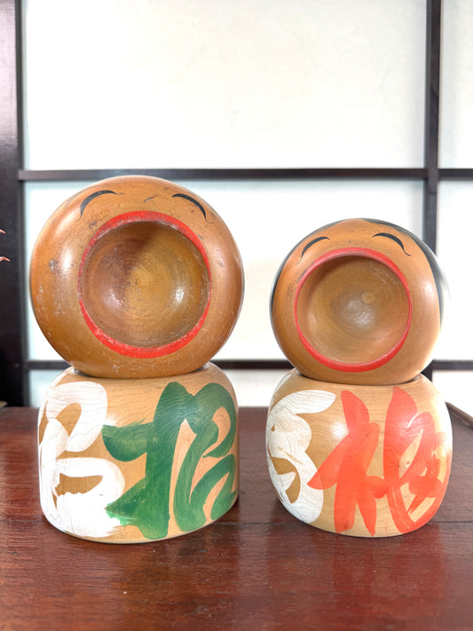 Couple de kokeshi rieuses en bois, calligraphie rouge et verte, signées Sato Kouson vu de face
