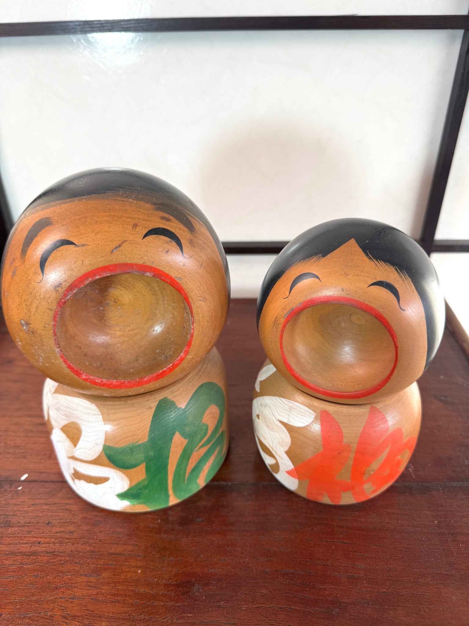 Couple de kokeshi rieuses en bois, calligraphie rouge et verte, signées Sato Kouson, vu de dessus