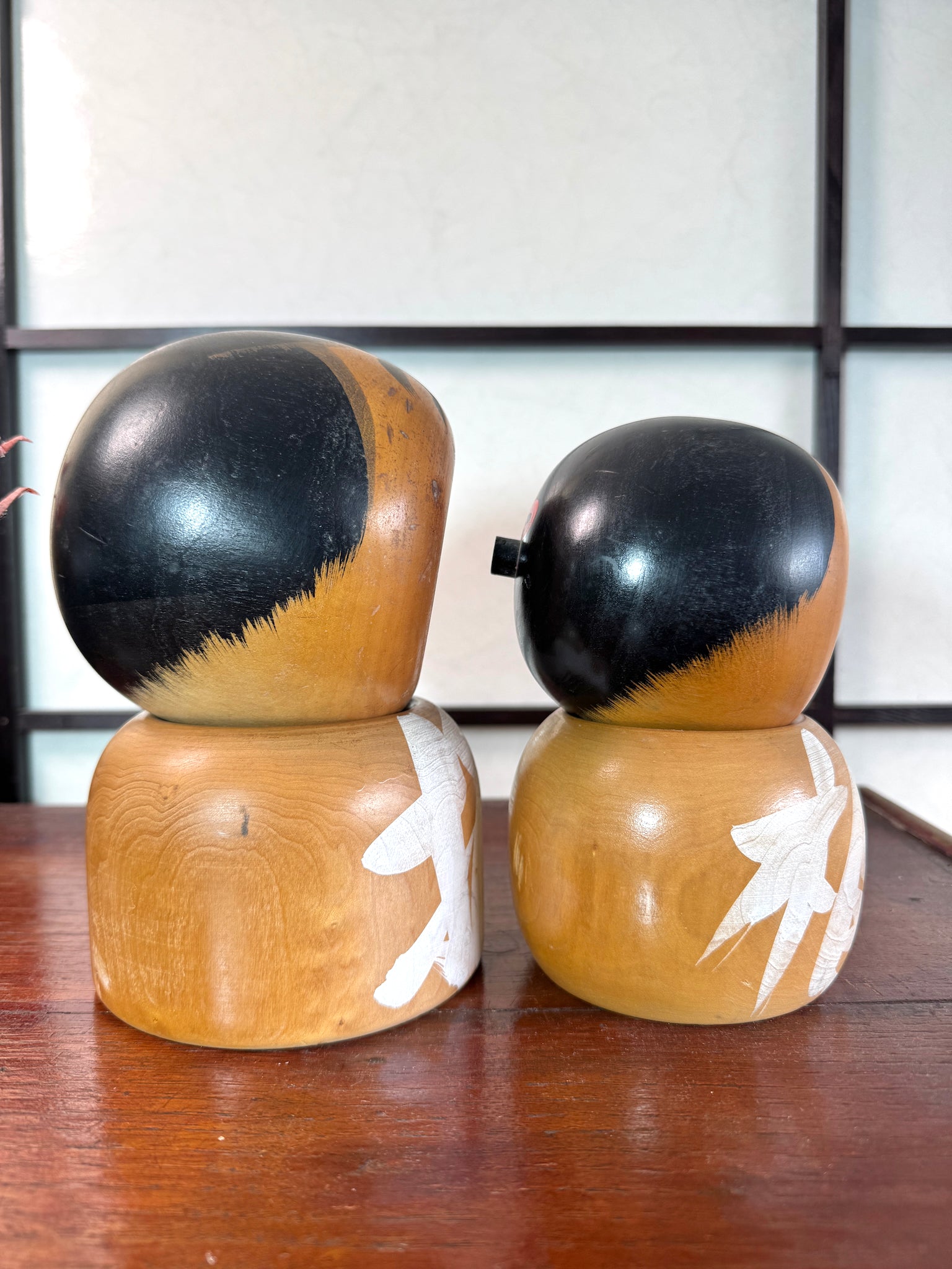 Couple de kokeshi rieuses en bois, calligraphie rouge et verte, signées Sato Kouson vu du profil droit