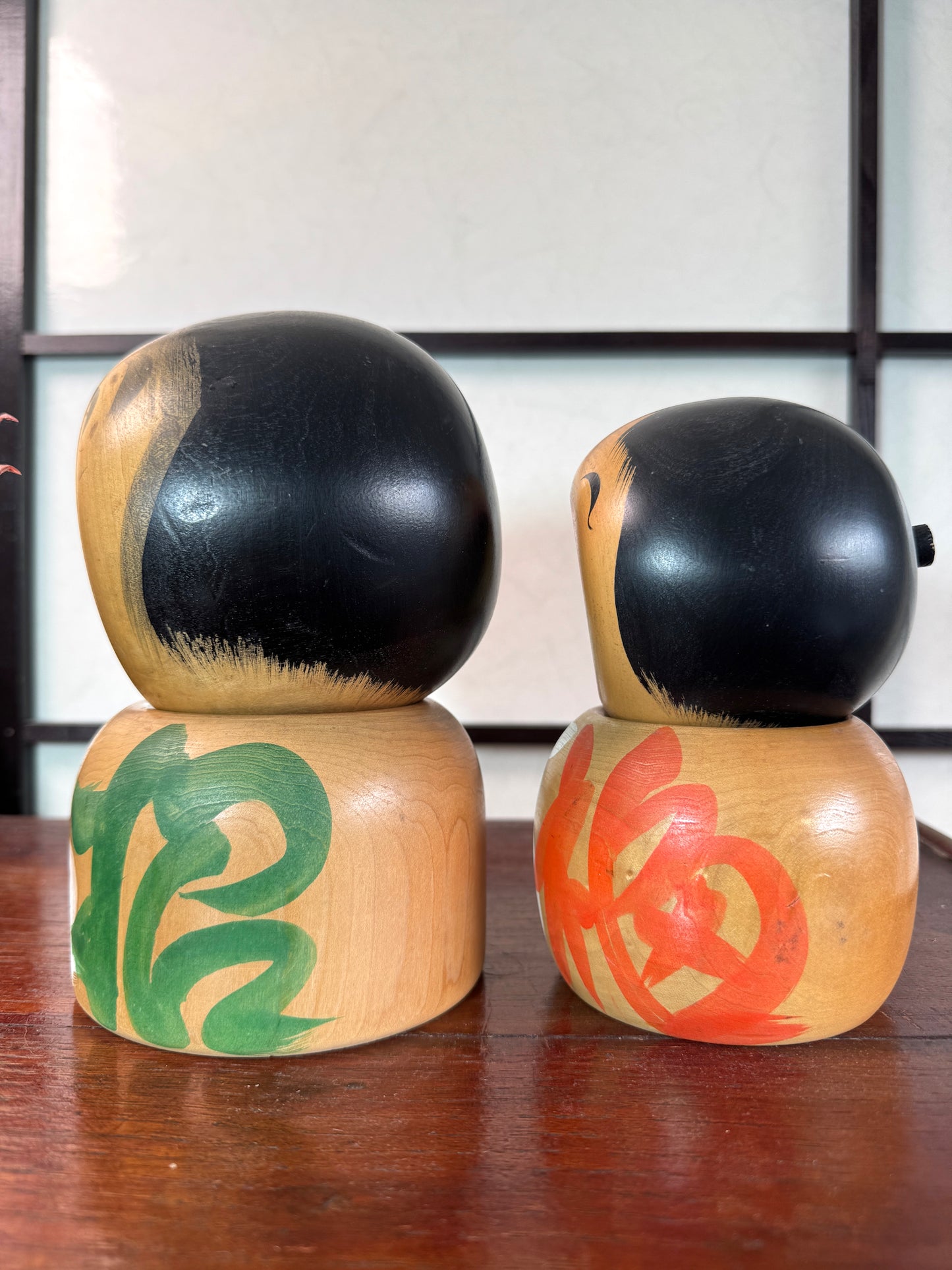 Couple de kokeshi rieuses en bois, calligraphie rouge et verte, signées Sato Kouson vu du profil gauche