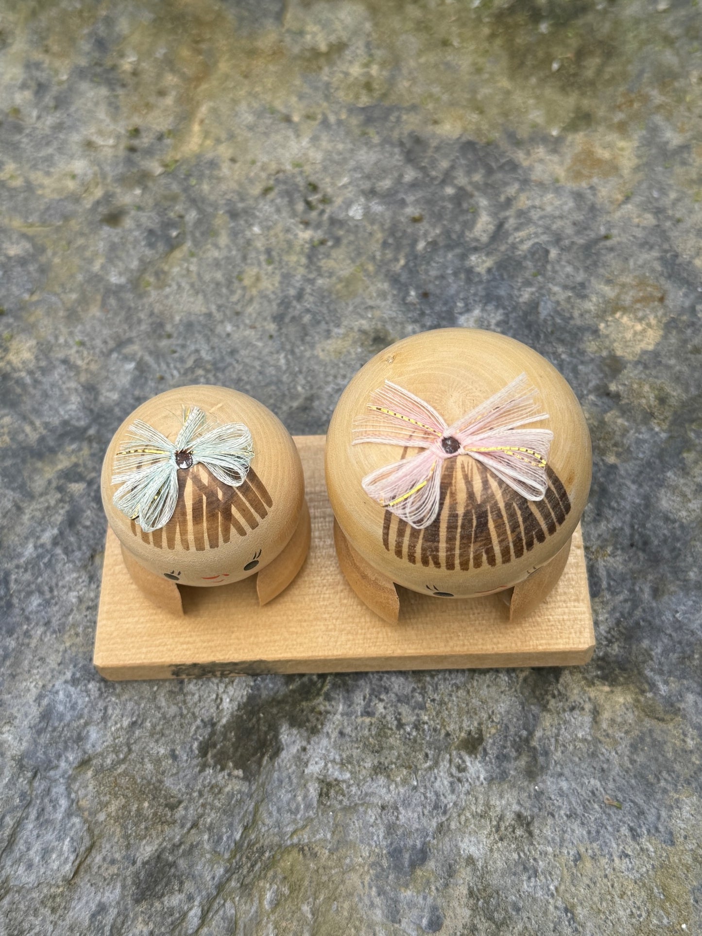 Couple de poupées kokeshi en bois sur socle, avec rubans rose et vert vue dessus