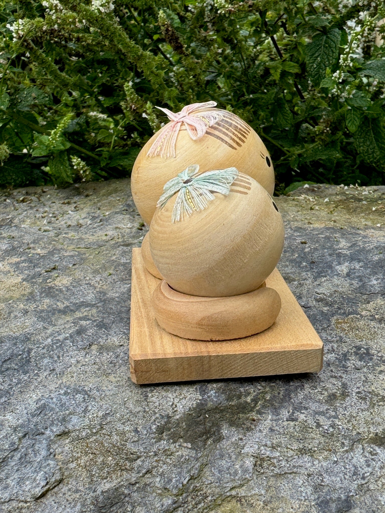 Couple de poupées kokeshi en bois sur socle, avec rubans rose et vert vue profil