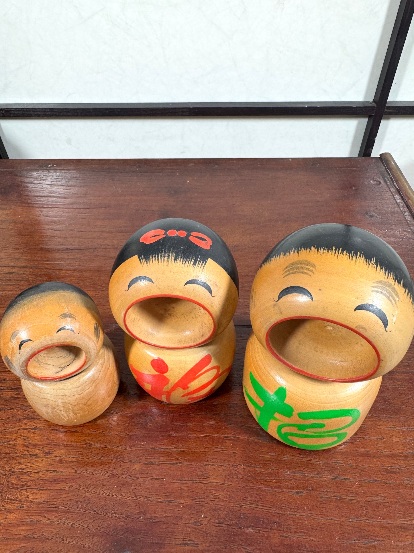 Trio de kokeshi en bois riant aux éclats avec calligraphie rouge et verte de Sato Kouson, vu de dessus