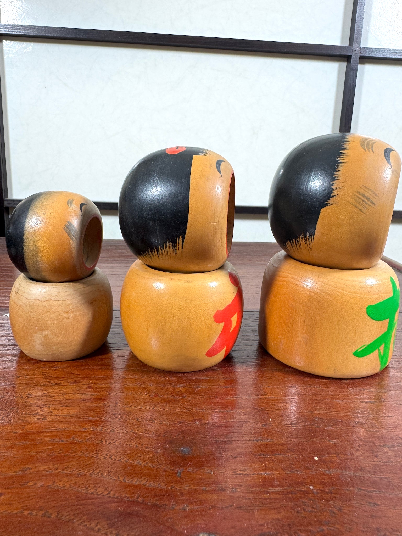 Trio de kokeshi en bois riant aux éclats avec calligraphie rouge et verte de Sato Kouson, profil droit