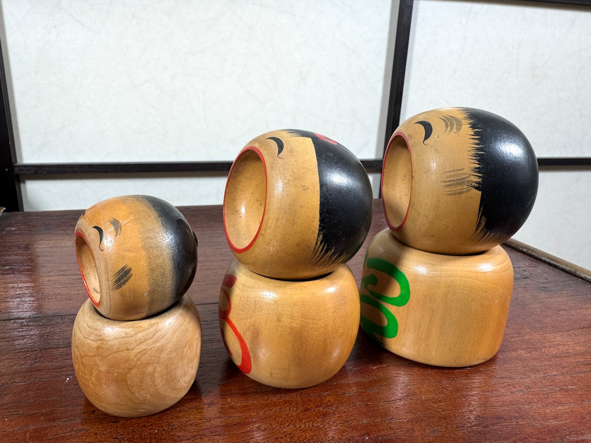 Trio de kokeshi en bois riant aux éclats avec calligraphie rouge et verte de Sato Kouson, profil gauche