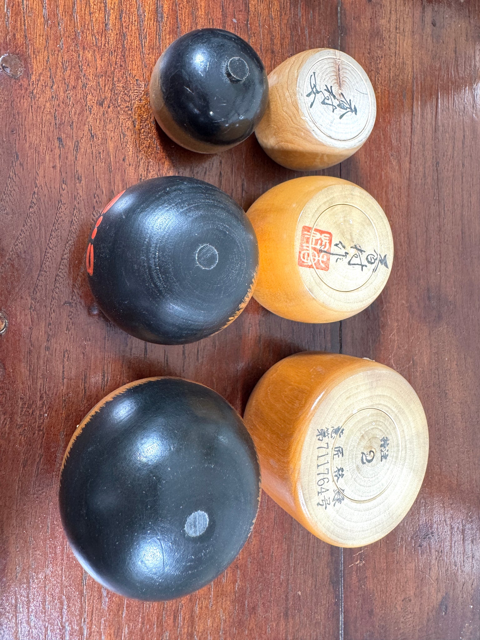 Trio de kokeshi en bois riant aux éclats avec calligraphie rouge et verte de Sato Kouson, vu de dessous avec la signature de l'artiste