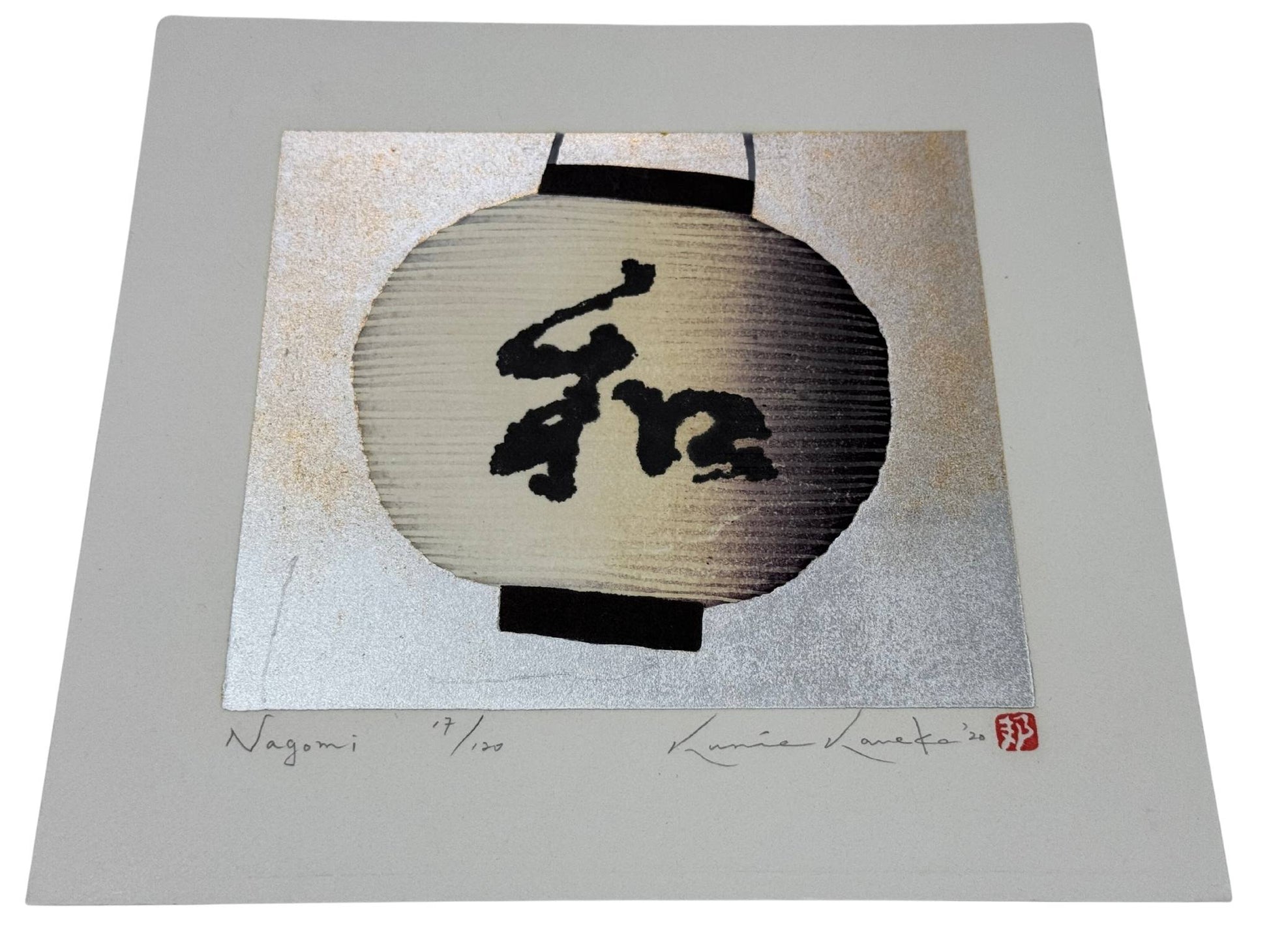 estampe japonaise de Kunio Kaneko représentant une lanterne japonaise ronde et blanche avec l'inscription nagomi en kanji, sur fond or et argent, le reflet du fond vu de profil