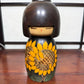 Kokeshi vintage japonaise de Yuji Kawase ornée de grands tournesols jaunes gravés et peints sur fond vert et noir.