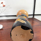 Grande kokeshi vintage de Yuji Kawase au corps noir décoré d’épis de riz beige, jaunes et rouges, Japon, période Shōwa. Le dessous