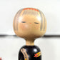 Grande kokeshi vintage de Yuji Kawase au corps noir décoré d’épis de riz beige, jaunes et rouges, Japon, période Shōwa. Gros plan sur le visage