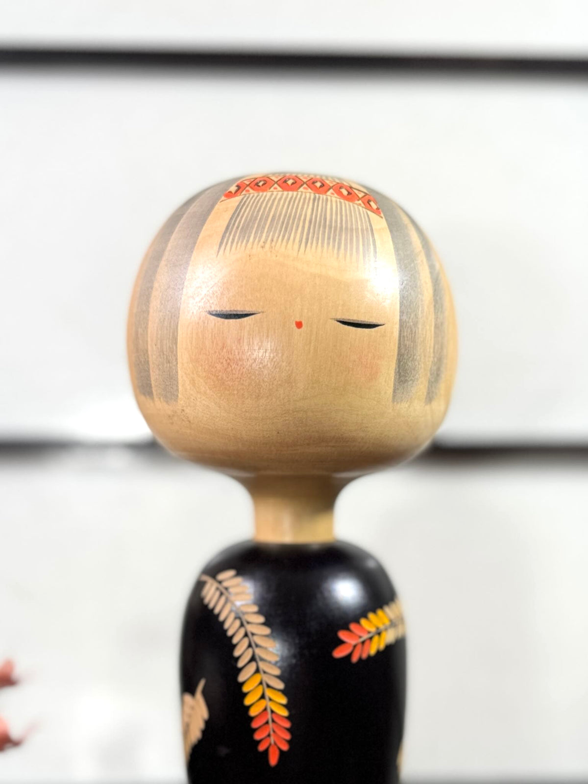 Grande kokeshi vintage de Yuji Kawase au corps noir décoré d’épis de riz beige, jaunes et rouges, Japon, période Shōwa. Gros plan sur le visage