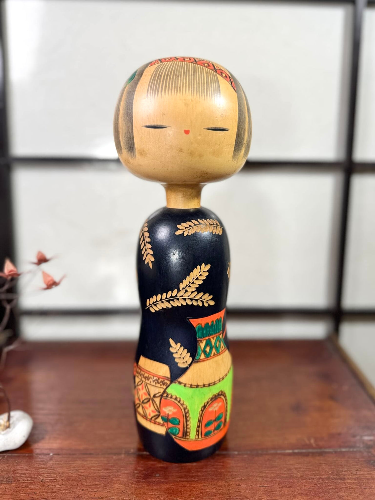 Kokeshi vintage de Yuji Kawase au corps noir décoré d’épis de riz et de deux récipients colorés à motifs géométriques.