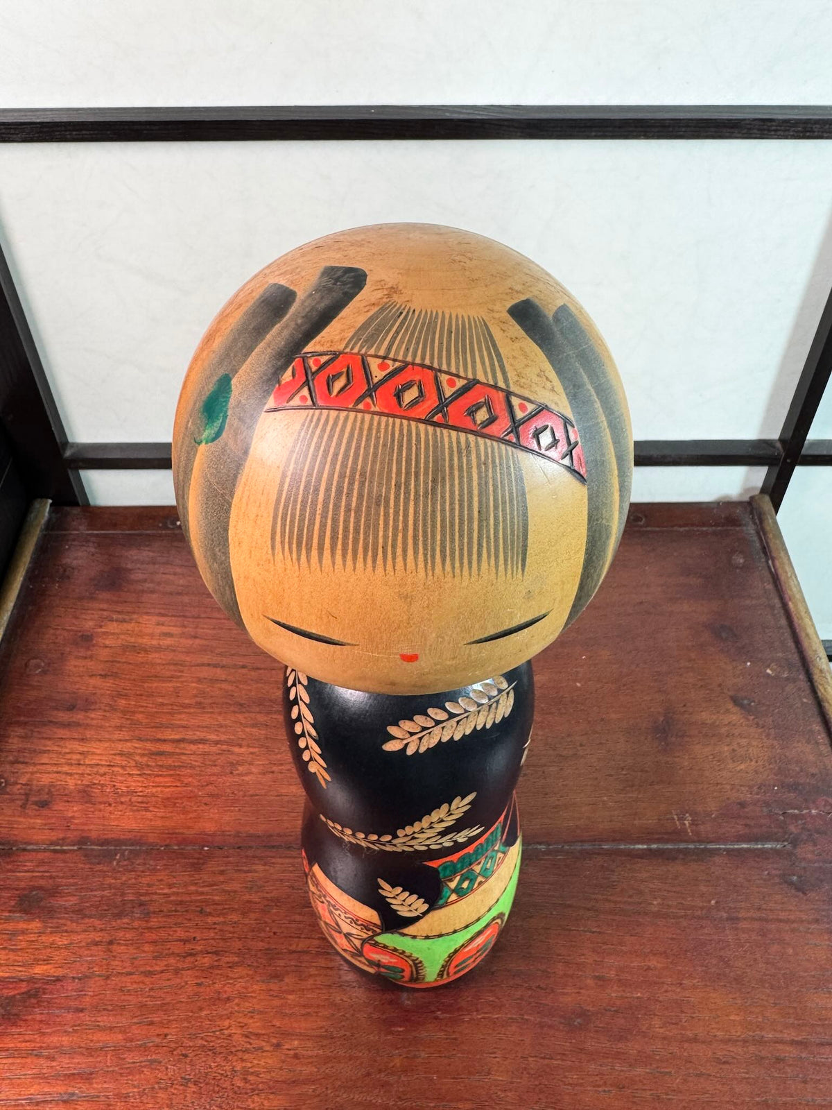 Kokeshi vintage de Yuji Kawase au corps noir décoré d’épis de riz et de deux récipients colorés à motifs géométriques, le dessus de la tête