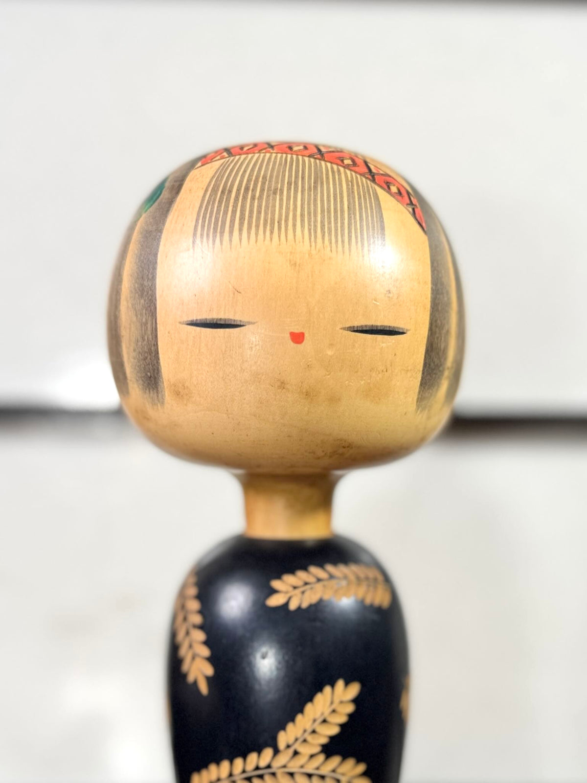 Kokeshi vintage de Yuji Kawase au corps noir décoré d’épis de riz et de deux récipients colorés à motifs géométriques, gros plan sur le visage