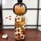Kokeshi vintage de Yuji Kawase datée de 1985, au petit chignon et kimono orné de fleurs blanches gravées évoquant le cerisier ou le prunier.