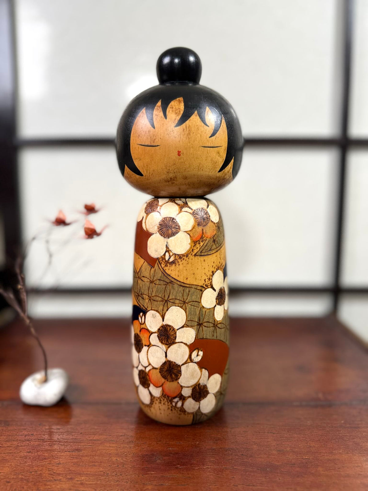 Kokeshi vintage de Yuji Kawase datée de 1985, au petit chignon et kimono orné de fleurs blanches gravées évoquant le cerisier ou le prunier.
