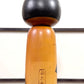 Kokeshi vintage de Yuji Kawase datée de 1985, au petit chignon et kimono orné de fleurs blanches gravées évoquant le cerisier ou le prunier, le dos avec la signature et la date pyrogravées