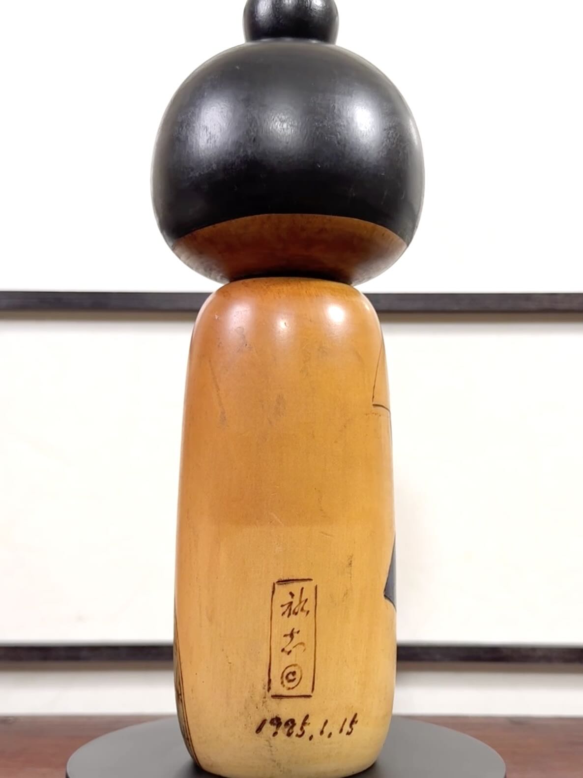 Kokeshi vintage de Yuji Kawase datée de 1985, au petit chignon et kimono orné de fleurs blanches gravées évoquant le cerisier ou le prunier, le dos avec la signature et la date pyrogravées