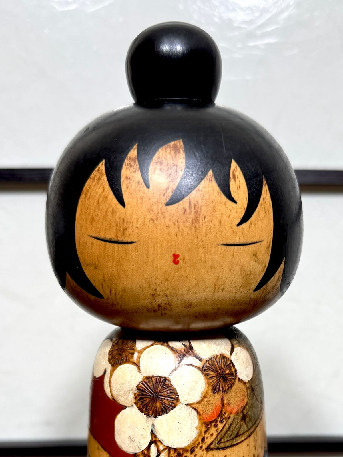 Kokeshi vintage de Yuji Kawase datée de 1985, au petit chignon et kimono orné de fleurs blanches gravées évoquant le cerisier ou le prunier, gros plan sur le visage