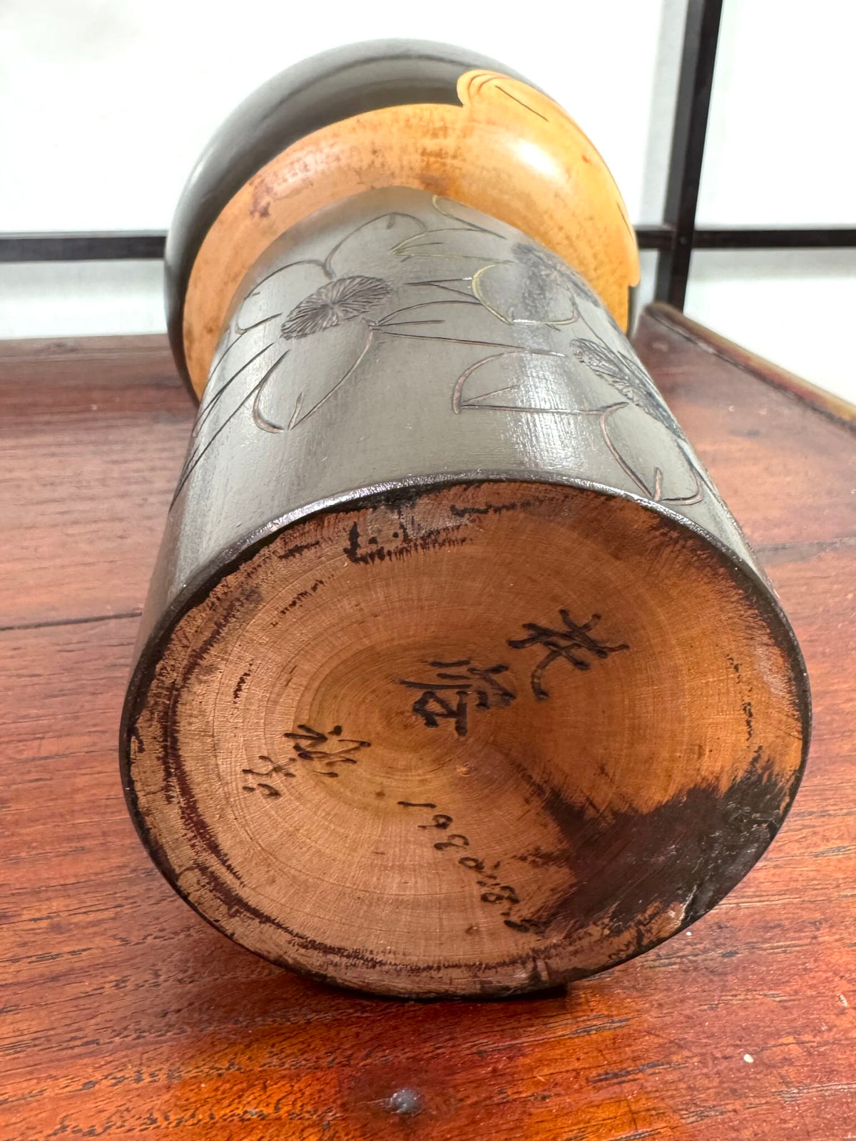 Kokeshi vintage de Yuji Kawase datée de 1980, caractérisée par une grande tête brune, un corps étroit et un décor de fleurs gravées, la signature et la date au dessous