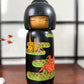 Kokeshi vintage de Yuji Kawase datée de 1992, décorée de grues en origami jaunes et rouges sur un corps noir.