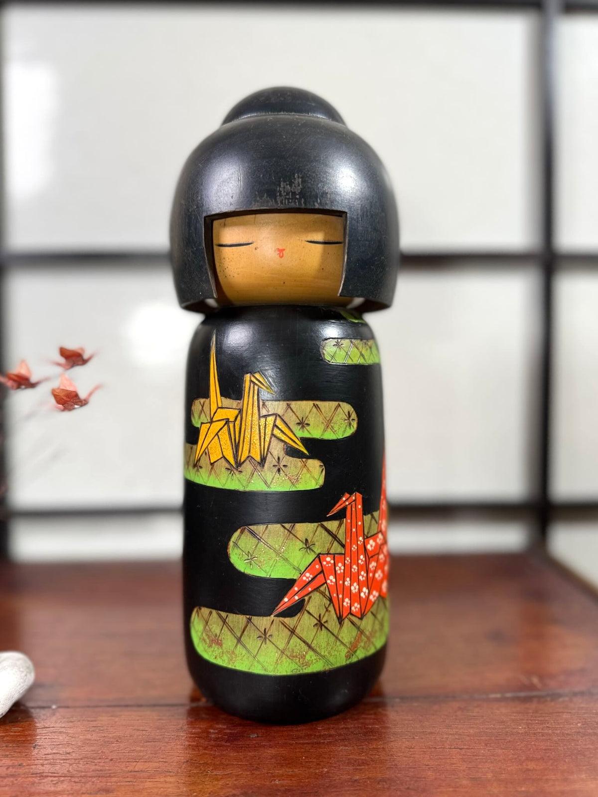Kokeshi vintage de Yuji Kawase datée de 1992, décorée de grues en origami jaunes et rouges sur un corps noir.