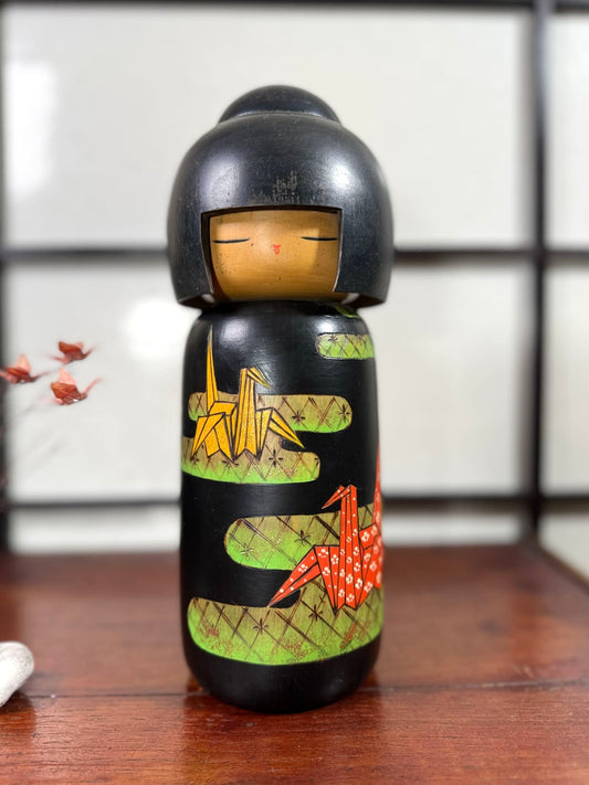 Kokeshi vintage de Yuji Kawase datée de 1992, décorée de grues en origami jaunes et rouges sur un corps noir.