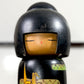 Kokeshi vintage de Yuji Kawase datée de 1992, décorée de grues en origami jaunes et rouges sur un corps noir, gros plan sur le visage