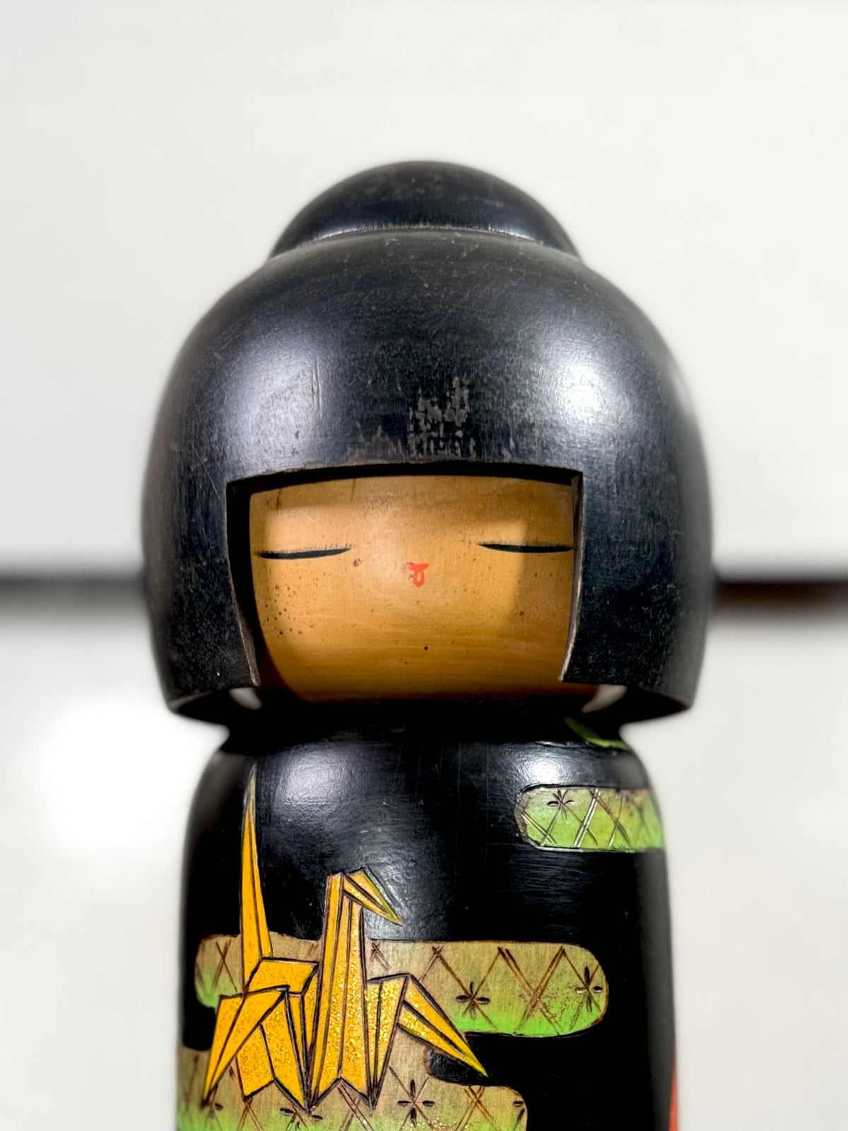 Kokeshi vintage de Yuji Kawase datée de 1992, décorée de grues en origami jaunes et rouges sur un corps noir, gros plan sur le visage