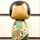 Kokeshi vintage de Yuji Kawase datée de 1994, au corps vert décoré de fleurs blanches et à la coiffure noire asymétrique.
