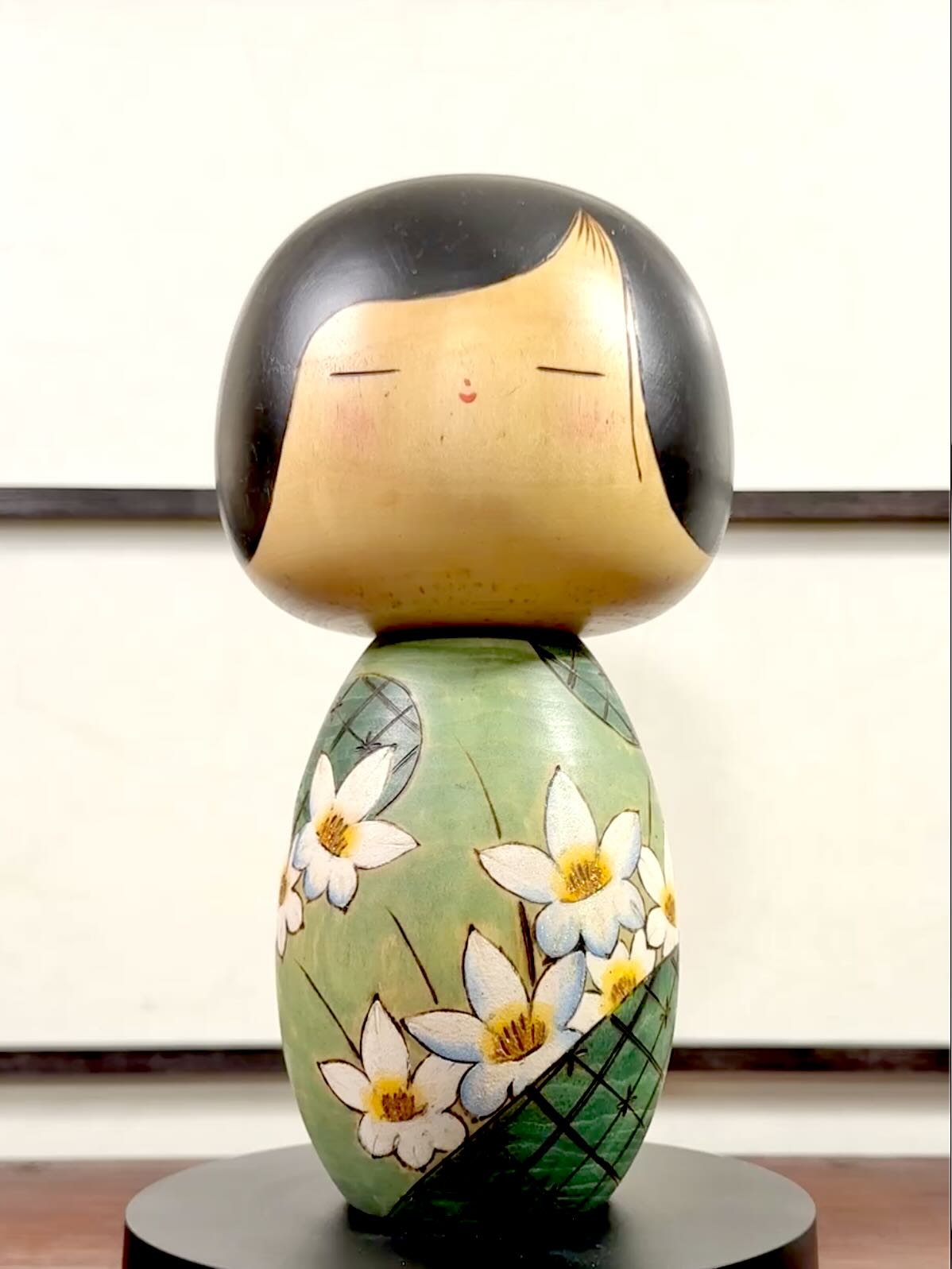 Kokeshi vintage de Yuji Kawase datée de 1994, au corps vert décoré de fleurs blanches et à la coiffure noire asymétrique.