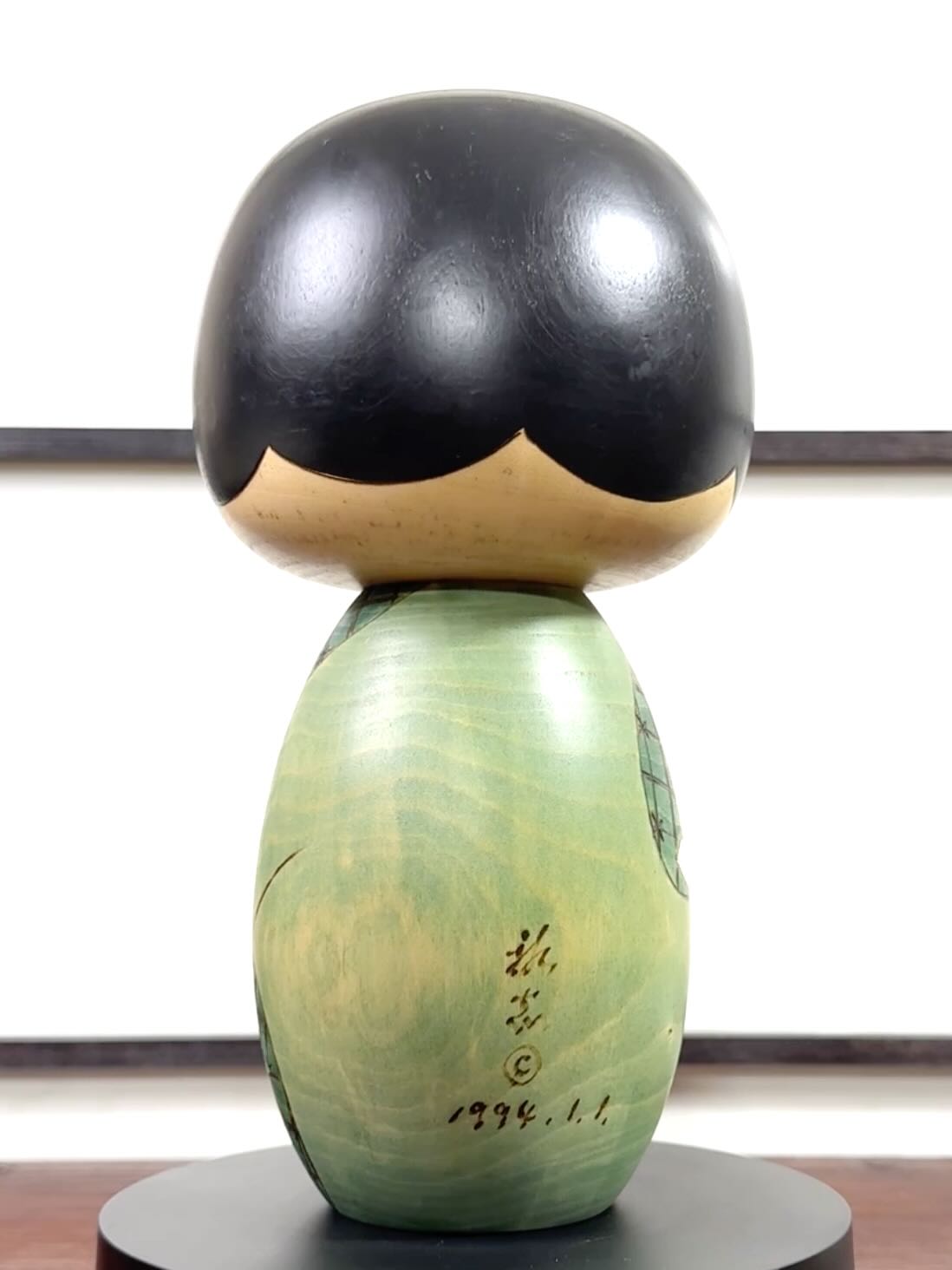 Kokeshi vintage de Yuji Kawase datée de 1994, au corps vert décoré de fleurs blanches et à la coiffure noire asymétrique, la signature et la date gravées au dos