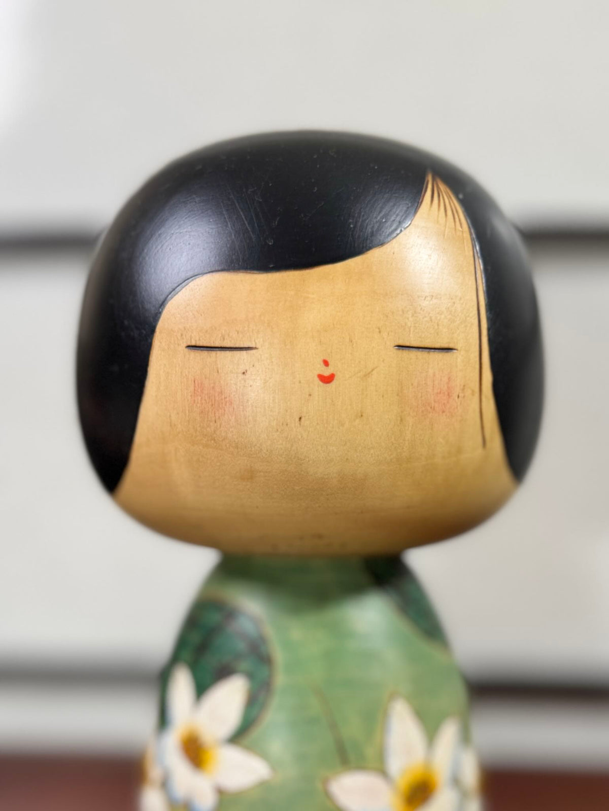 Kokeshi vintage de Yuji Kawase datée de 1994, au corps vert décoré de fleurs blanches et à la coiffure noire asymétrique, gros plan sur le visage souriant